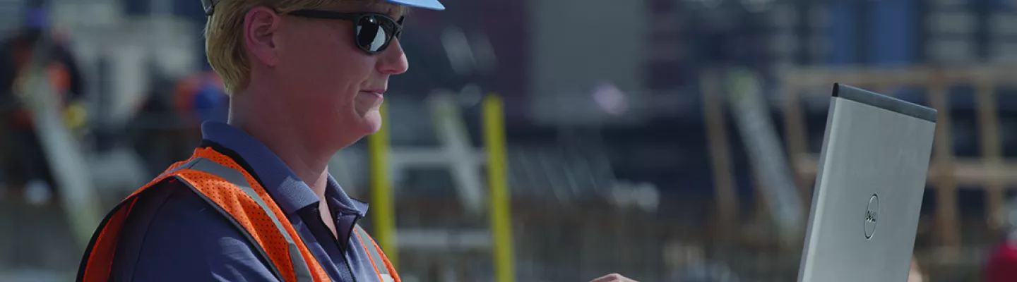 female in hardhat on construction site with laptop