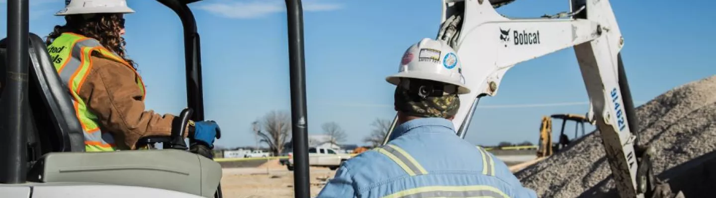 woman in mini excavator next to man near dirt pile