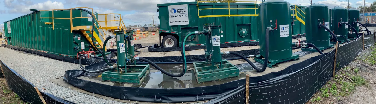 green tanks and pumps handling water discharge at a jobsite on a clear day