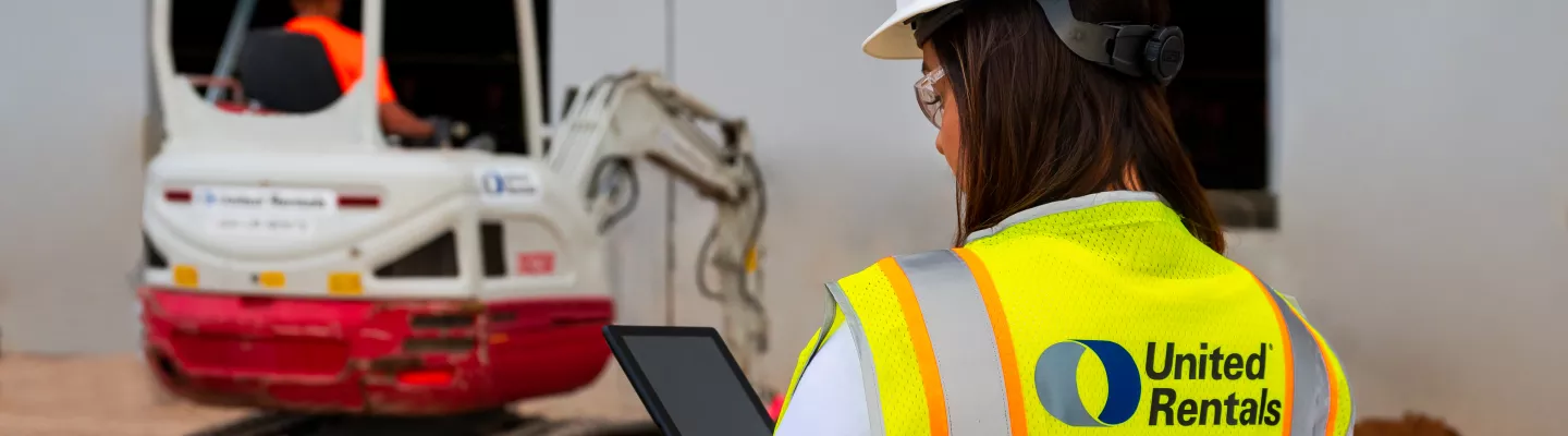 woman on jobsite holding ipad next to skid steer
