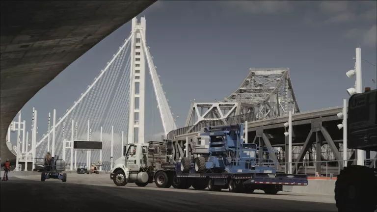truck hauling blue equipment to a large bridge
