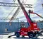 Side view of a red Magni telehandler with extended boom, stabilizers, enclosed cabin, working on a snowy construction site.