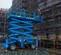 Side view of a blue partially extended Genie scissor lift with worker in safety gear next to construction building exterior.