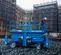 Side view of a blue Genie scissor lift with an operator in safety gear on the platform at an active construction site.