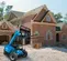 Front angled view of a blue Genie telehandler with extended boom and forklift attachment outdoors on in front of a house.