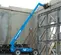 Side view of a blue Genie telehandler with an extended boom with an enclosed cabin in use on a construction site.