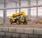Front angled view of yellow JCB telehandler with retracted boom lifting pallets of construction material on a worksite.