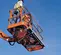 Bottom up angled view of two workers in safety gear in a scissor lift basket, elevated on a clear blue sky background.