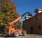 Rear angled view of an orange SkyTrack telehandler with extended boom lifting materials to the roof of a building outdoors.