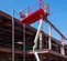 Side view of a red and white rough terrain scissor lift at a construction site.
