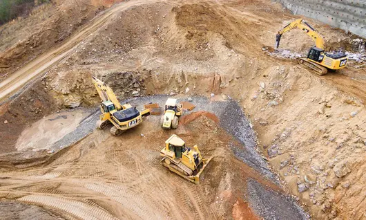 Excavators assisting construction crews on-site, with safety barriers in place to control access and protect workers.







