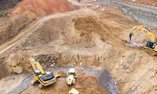 "Excavators assisting construction crews on-site, with safety barriers in place to control access and protect workers."







