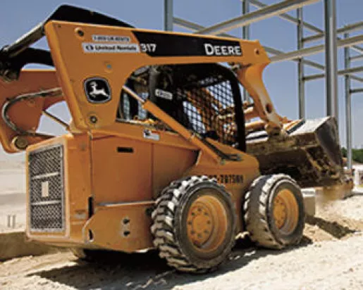 yellow john deere skid steer on jobsite in front of framed building