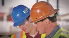 3 men looking at computer screen, one man pointing. All men are wearing hats and safety glasses