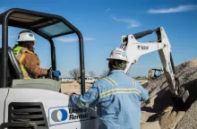 woman in mini excavator next to man near dirt pile