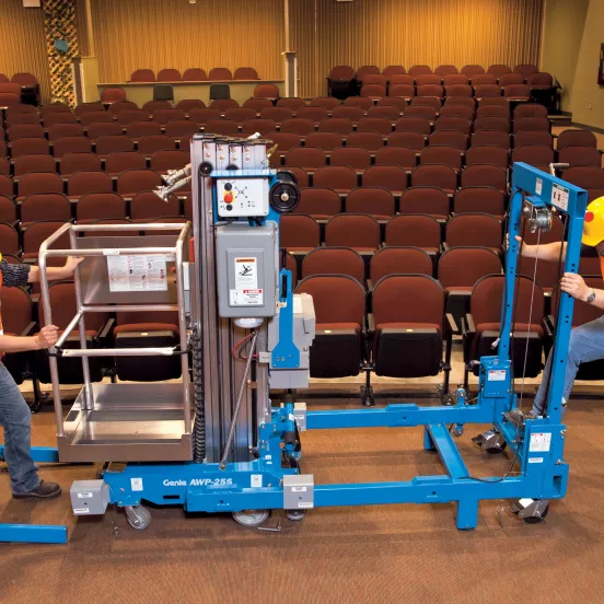 Side view of a blue Genie straddle kit for pusharund lift with arm retracted, idle on a stage in an auditorium.